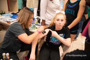 Autumn applying a sparkle breast cancer ribbon to Excel Cheerleader.